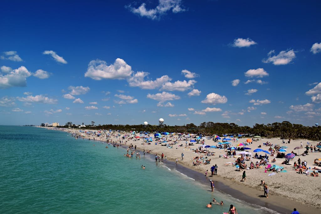 Crowds enjoy a sunny day at Venice Beach, Florida with clear skies and vibrant beach umbrellas.