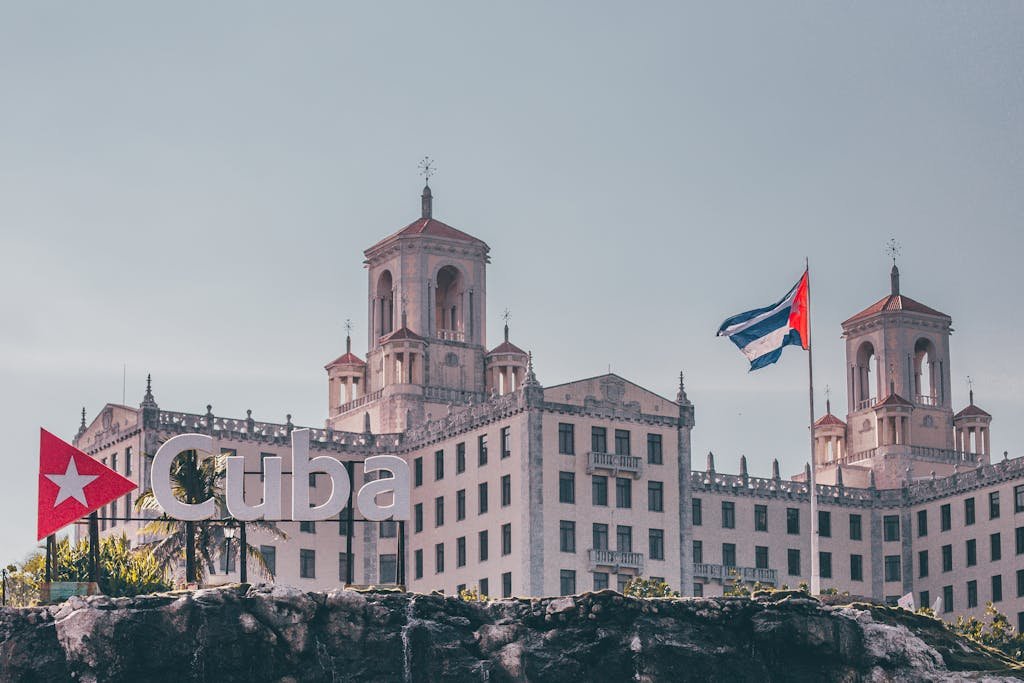 View of the historic Hotel Nacional in Havana, Cuba with a waving Cuban flag and clear sky.