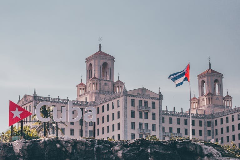 View of the historic Hotel Nacional in Havana, Cuba with a waving Cuban flag and clear sky.