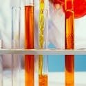 Close-up of a lab technician pouring orange liquid into test tubes in a laboratory setting.