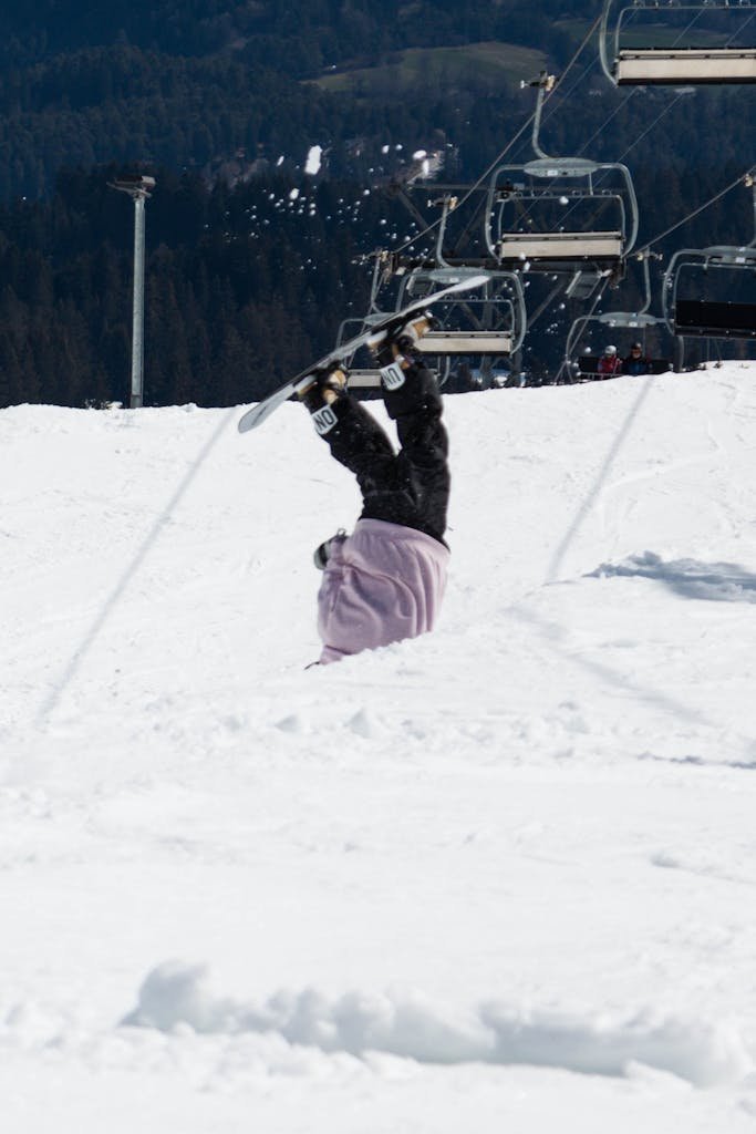 Snowboarder falls headfirst in snowy Swiss Alps landscape with chairlift in background