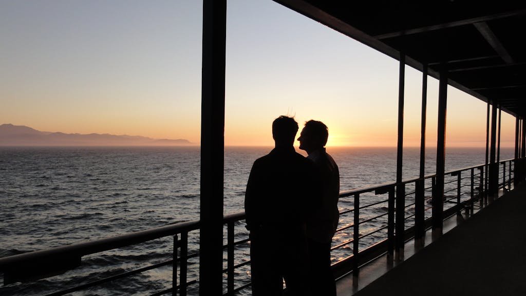 Silhouettes of a couple on a ship deck enjoying a breathtaking sunset over the ocean.