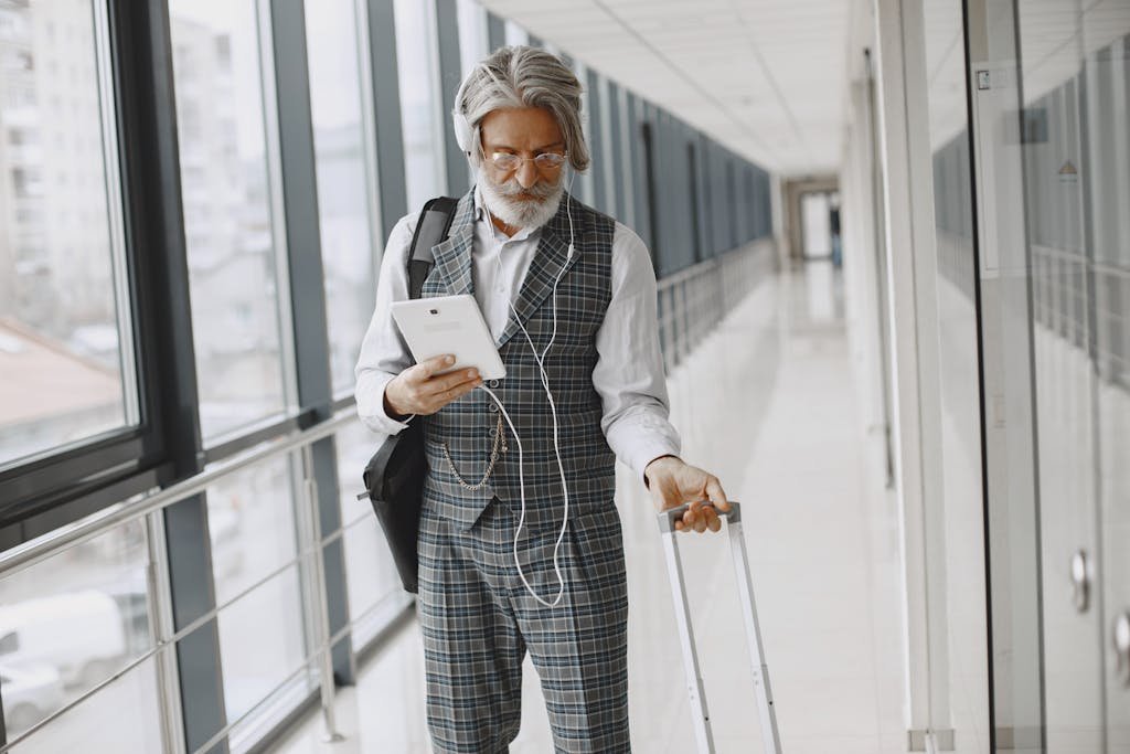 Senior man with gray hair traveling, using tablet in modern hallway.