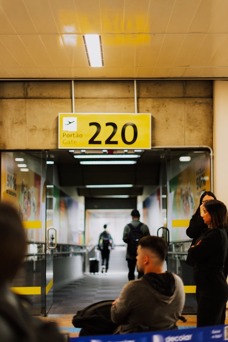 Travelers waiting at a bustling airport gate with a focus on the entrance and sign.