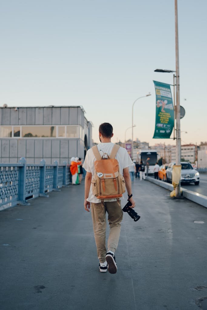 Backpacker crossing a city bridge during daytime. Capturing moments with a camera in hand.