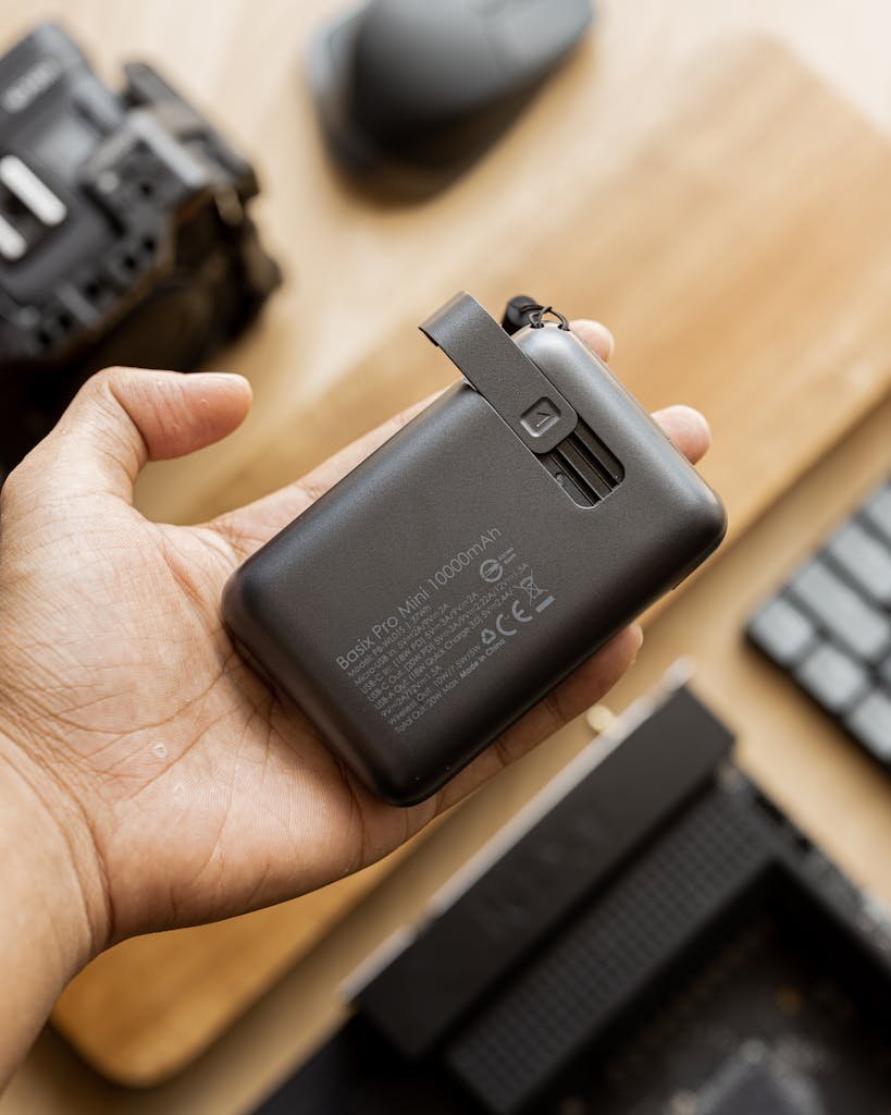 Person holding a compact external hard drive on a desk with tech gadgets around.