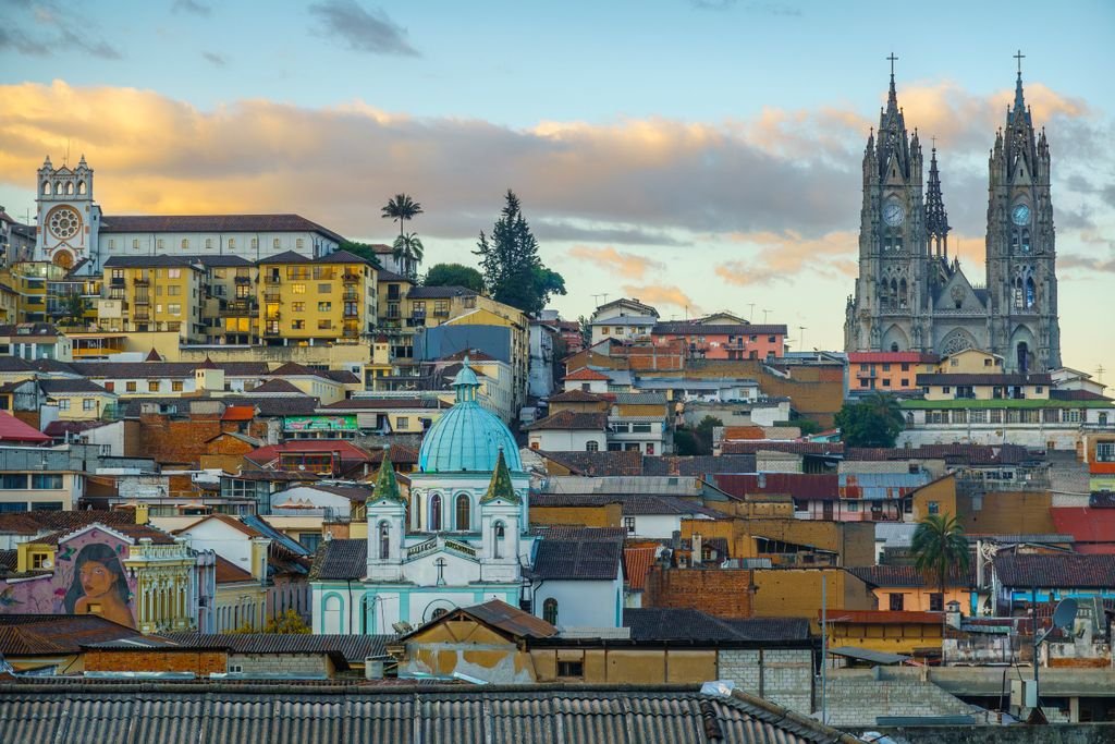 A scenic view of Quito's historic skyline with iconic churches and colorful architecture at sunset.