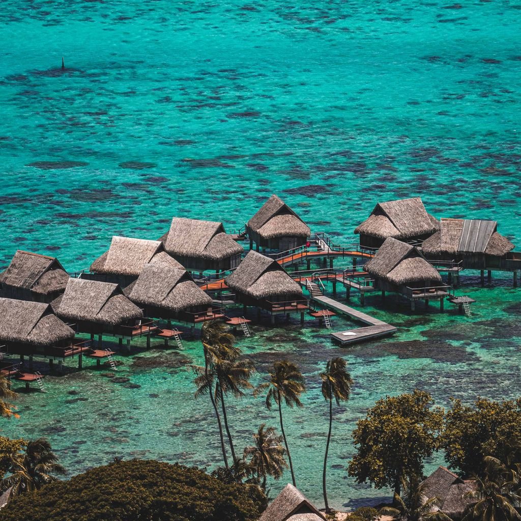 Aerial view of scenic overwater bungalows in a tropical turquoise ocean with lush palm trees.