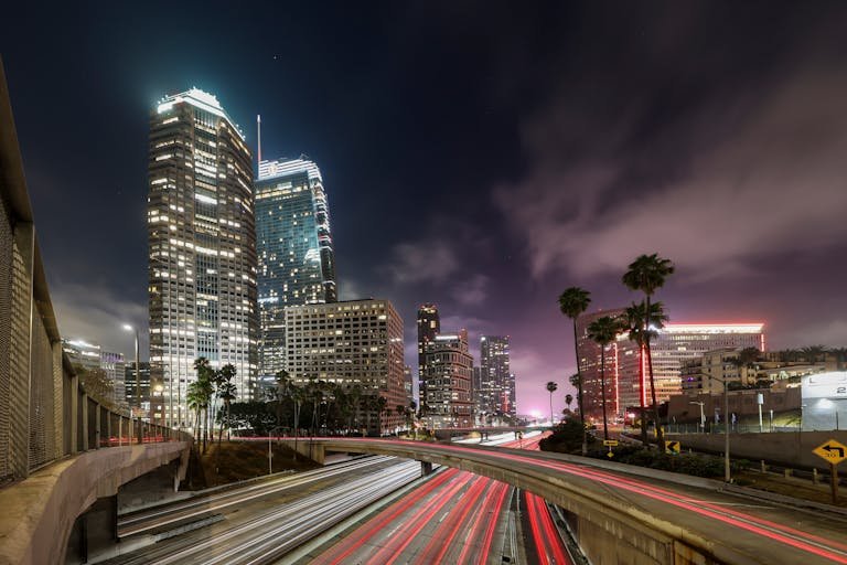 Stunning long-exposure night shot of Los Angeles skyline with illuminated highways and towering buildings.