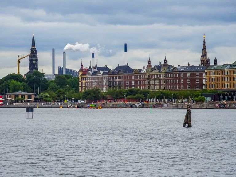 View of Copenhagen's riverside with historic architecture and urban skyline on a cloudy day.