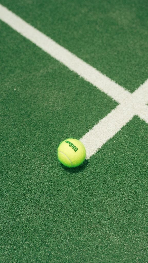 Close-up of a tennis ball on a green court with white lines, outdoor sports theme.