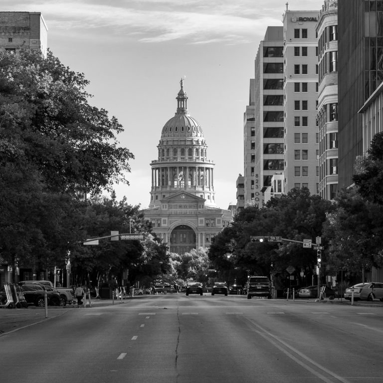 Monochrome image featuring the Texas State Capitol in Austin with a lined street view.