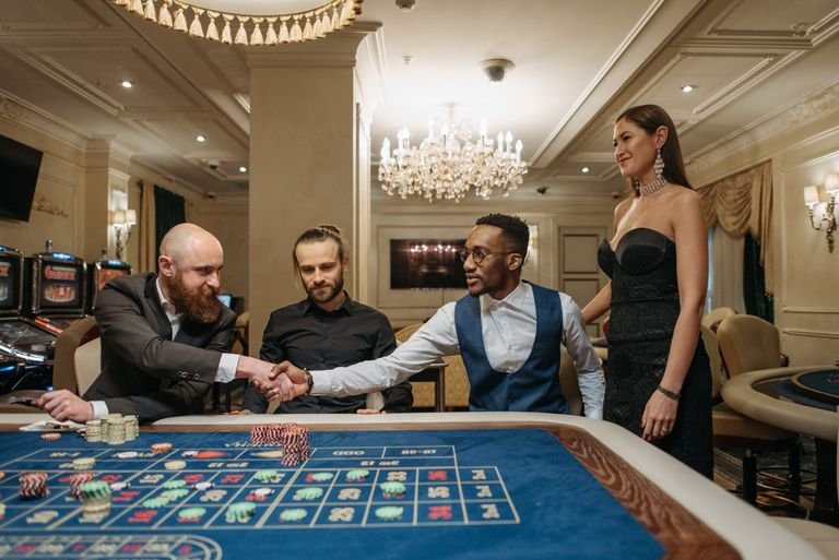 Group of diverse adults engaged at a luxurious casino, shaking hands over a roulette table.