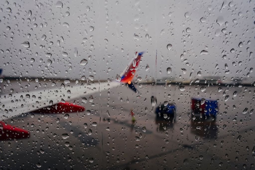 Raindrops on a airport runway during a weather delay with planes waiting at the gates