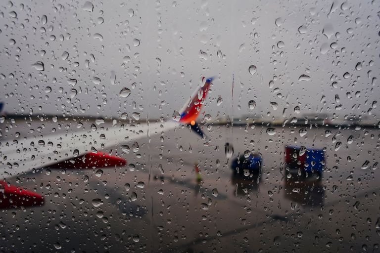 Raindrops on a airport runway during a weather delay with planes waiting at the gates